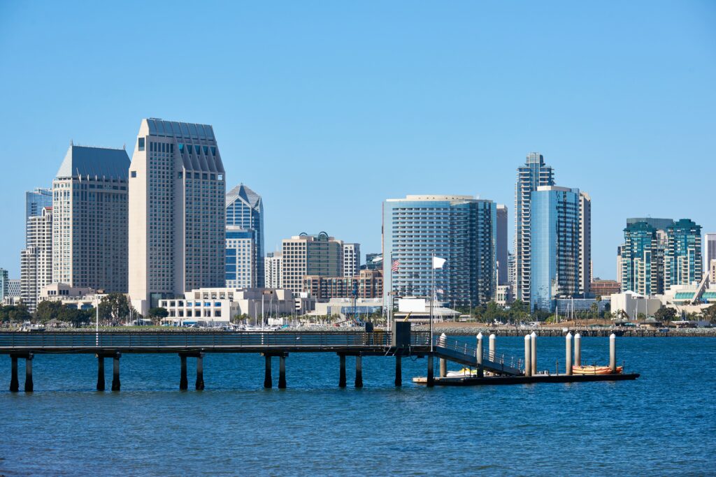 Kayak boats at a pier with the San Diego skyline in the background during sunset, representing coastal vehicle shipping services.